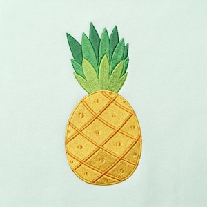Puede incluir: Un diseño de piña bordado sobre un fondo de tela verde menta claro. La piña presenta un cuerpo amarillo dorado con un patrón de diamantes entrecruzados y una parte superior de hojas verdes vibrantes con frondas puntiagudas y superpuestas.