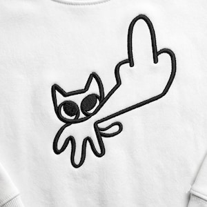 May include: A white sweatshirt featuring a black embroidered line art design of a cat with large eyes. The cat is depicted with one of its limbs extended upward in a gesture resembling a middle finger. The embroidery is clean and centered.