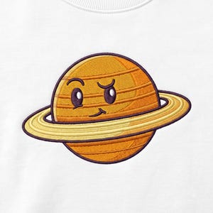 May include: A white t-shirt featuring an embroidered graphic of a cartoon planet Saturn. The planet is orange with horizontal lines, a light yellow ring, and a dark purple outline. It has a facial expression with raised eyebrows and a smirk.