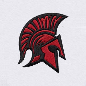 Puede incluir: Un parche bordado que presenta un diseño de casco espartano estilizado en hilo rojo y negro intenso. El casco se muestra de perfil, destacando una cresta prominente y un protector facial, todo sobre un fondo de tela blanca lisa.