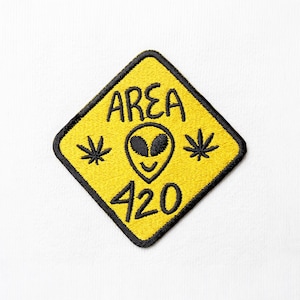 May include: A diamond-shaped embroidered patch with a yellow background and a thick black border. The patch features the black embroidered text AREA 420, a central alien head icon, and two small cannabis leaf symbols on either side of the alien.
