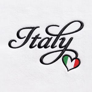 May include: A white fabric surface featuring black embroidered cursive text that reads Italy. The letter y extends into a heart shape at the bottom right, which is filled with vertical stripes of green, white, and red embroidery thread.