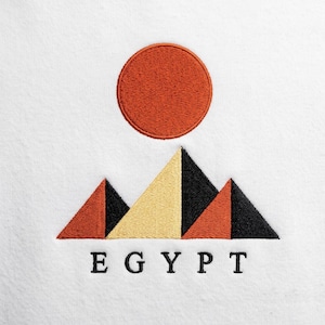 Può includere: Una superficie in tessuto bianco con un ricamo raffigurante un cerchio arancione pieno sopra tre triangoli geometrici nei toni dell'arancione, giallo e nero. La parola EGYPT è ricamata in lettere maiuscole nere sotto i triangoli.