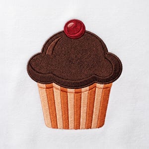 Op de afbeelding: Een geborduurd cupcake-ontwerp met donkerbruin glazuur en een enkele rode kers als topping. De basis van de cupcake heeft verticale strepen in afwisselende tinten lichtbruin en oranje, geborduurd op een effen witte stoffen ondergrond.
