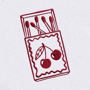 May include: A white fabric surface featuring a red embroidered design of an open matchbox. The matchbox displays a central illustration of two cherries with a leaf, surrounded by a wavy border, with several matches protruding from the top.