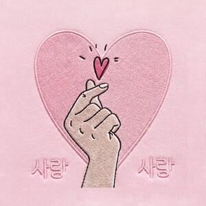 Puede incluir: Una tela rosa claro con un diseño bordado de una mano haciendo un gesto de corazón con los dedos frente a un gran corazón rosa. Sobre el corazón de los dedos hay un pequeño corazón rosa oscuro. El texto coreano 사랑 está bordado a ambos lados.
