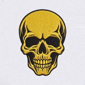 Puede incluir: Un parche bordado con un diseño de cráneo humano estilizado. El cráneo está realizado con hilo amarillo vibrante, con detalles en hilo negro profundo que definen las cuencas de los ojos, la cavidad nasal y los espacios entre los dientes.