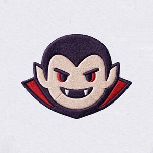 May include: An embroidered patch featuring a stylized vampire head with dark purple hair, pale skin, and red eyes. The figure has a wide grin showing two white fangs and is wearing a high-collared cape with a vibrant red interior lining.