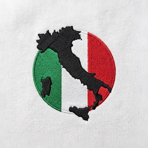 May include: A circular embroidered patch on a white fabric background featuring a black silhouette of the Italian peninsula map overlaid on a vertical tricolor flag design consisting of green, white, and red stripes with stitched texture.