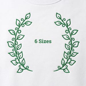 May include: A white fabric surface featuring two symmetrical green embroidered leafy branches facing each other. The text 6 Sizes is embroidered in green between the two branches. The design consists of curved stems and pointed leaves.