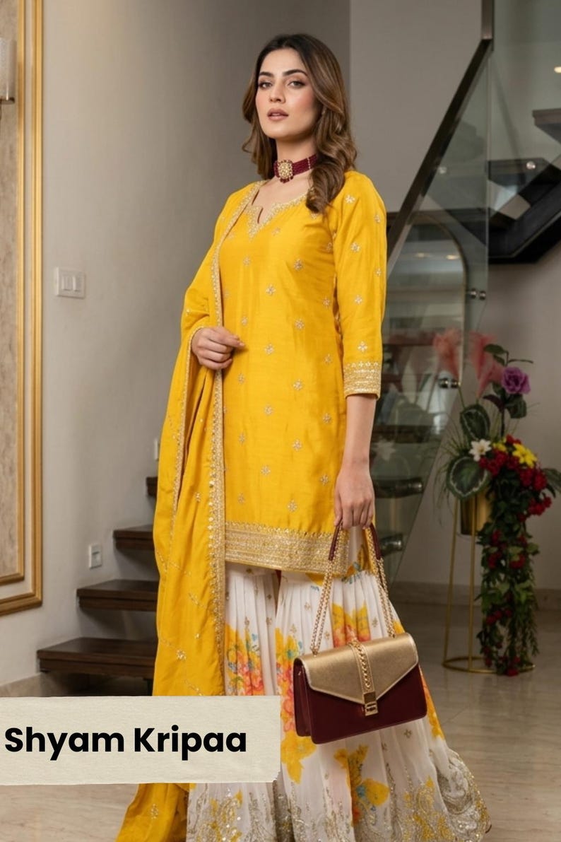 May include: A yellow kurta with gold embroidery, paired with a white and yellow floral print sharara and a matching dupatta. The outfit is accessorized with a maroon and gold handbag. The text Shyam Kripaa is visible in the bottom left corner.
