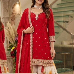 May include: A red kurta with three-quarter sleeves, a scalloped neckline, and gold embroidery, paired with a white floral print skirt and a matching red dupatta with a gold border. The text Shyam Kripaa is visible at the bottom of the image.
