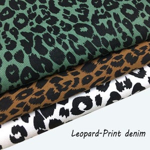 May include: Three folded layers of denim fabric featuring a black leopard print pattern. The top layer is sage green, the middle layer is tan brown, and the bottom layer is white. The text "Leopard-Print denim" is printed in the bottom right corner.