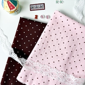 May include: Two folded pieces of fabric, one dark brown with white polka dots and one light pink with dark brown polka dots, accented by a strip of white floral lace trim, a small carousel trinket box, and several small decorative craft embellishments.