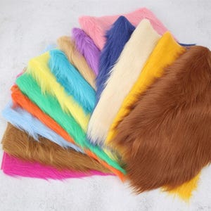 Könnte beinhalten: Eine Sammlung rechteckiger Kunstfell-Stoffmuster, die fächerförmig angeordnet sind. Die Farben umfassen leuchtendes Pink, Braun, Hellblau, Orange, Grün, Gelb, Türkis, Beige, Violett, Dunkelblau, Creme und Gold, alle mit langen Fasern.