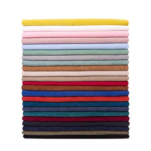 May include: A vertical stack of twenty-five folded fabric pieces featuring a distinct corduroy texture. The collection displays a wide spectrum of colors including yellow, white, pink, light blue, sage green, grey, tan, brown, red, blue, and black.