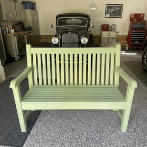 May include: A light green wooden bench featuring a slatted backrest and a slatted seat. The bench has two armrests and four straight legs, constructed with a simple frame design. The finish is a solid, matte light green color throughout.