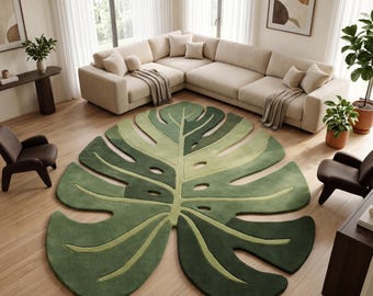 May include: A large area rug shaped like a monstera leaf, featuring a gradient of dark and light green tones with cut-out details along the edges. The rug has a textured surface and follows the organic, lobed silhouette of a tropical plant leaf.