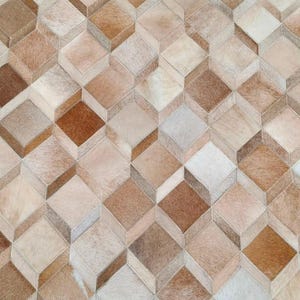May include: A rug constructed from individual pieces of cowhide leather arranged in a repeating geometric pattern of three-dimensional cubes. The surface features varying shades of brown, tan, cream, and white hair-on-hide textures.