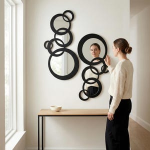 Peut inclure: Deux miroirs décoratifs muraux dotés d'un cadre noir composé de multiples formes circulaires interconnectées de tailles variées. Le design comprend plusieurs anneaux ouverts et deux surfaces de miroir circulaires intégrées à l'ensemble.