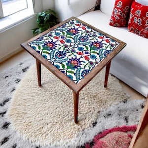 May include: A square wooden side table featuring a flat top surface decorated with a vibrant floral pattern in shades of blue, red, and green on a white background. The table is supported by four tapered wooden legs and has a dark wood frame.