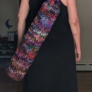 May include: A person wearing a black dress carrying a colorful crocheted yoga mat bag.