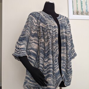 May include: A blue and white striped knitted cardigan with a loose fit and open front. The cardigan has a delicate stitch pattern and a slightly flared hem.