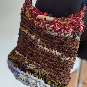 May include: A brown crocheted bag with a wooden toggle closure. The bag is made from recycled fabric scraps and has a multi-colored striped pattern.