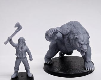 May include: A gray unpainted miniature figure of a bearded human holding an axe raised in one hand, standing on a black circular base, positioned next to a larger gray unpainted miniature figure of a bear in a charging pose on a black base.