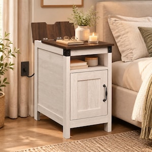 May include: A white wooden end table with a dark brown top that features a hinged lid, an open storage shelf containing two books and a small container, and a lower cabinet door with a black metal handle. The table has a power cord attached.