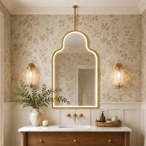 May include: A bathroom vanity featuring a wooden cabinet with three drawers, a white marble countertop, and a gold faucet. Above the vanity is a gold-framed arched mirror with integrated LED lighting, flanked by two vertical glass wall sconces.