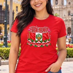 May include: A red short-sleeved t-shirt featuring a graphic print of the Peruvian flag, the word PERU in white stylized lettering, and a decorative border of red and white cantuta flowers with small pink hearts and sparkles.