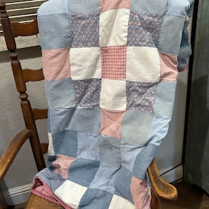 May include: A patchwork quilt featuring a grid of square fabric panels in shades of light blue, denim blue, white, and muted red. The quilt includes solid denim squares, white squares, and patterned squares with small floral or plaid designs.