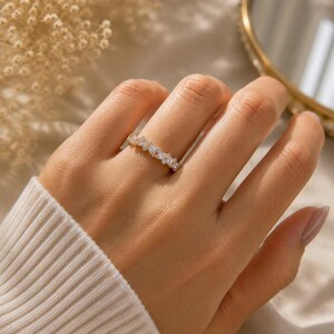 May include: A gold-toned ring featuring a series of marquise-cut clear stones arranged in a continuous band. The stones are set in a delicate metal frame that follows the finger, creating a sparkling, textured appearance across the band's surface.