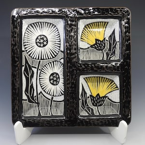 May include: A square ceramic serving tray with a glossy black textured border and three recessed compartments. The left section features two black and white dandelion illustrations, while the two right sections display yellow and black flower motifs.
