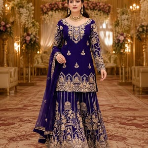 May include: A deep blue sharara suit featuring intricate gold embroidery on the long-sleeved tunic and wide-leg trousers. The ensemble includes a matching sheer dupatta with gold border detailing, creating a cohesive look with ornate patterns.