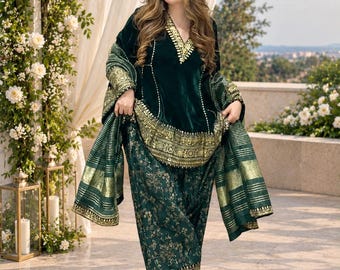 May include: A dark green velvet tunic with a V-neckline and gold embroidery, paired with matching green trousers featuring a gold floral print and a wide gold border. A coordinating green shawl with gold stripes is draped over the arms.