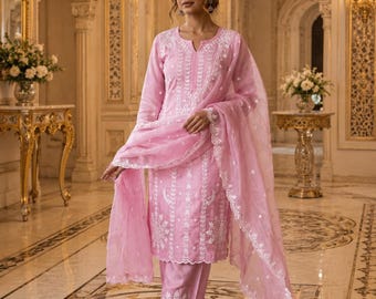 May include: A light pink three-piece outfit consisting of a long-sleeved tunic, straight-leg trousers, and a matching sheer dupatta. The tunic and trousers feature intricate white floral embroidery, while the dupatta has a scalloped lace border.