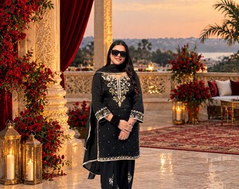 May include: A black salwar kameez set featuring intricate gold embroidery along the neckline, cuffs, and hem. The outfit includes a matching black dupatta with a gold border, paired with black trousers and pointed metallic silver shoes.
