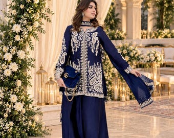May include: A deep navy blue long-sleeved tunic and matching wide-leg trousers set featuring intricate white embroidery along the front, cuffs, and hem. The outfit includes a coordinating navy blue scarf and a dark blue velvet handbag with a gold chain.