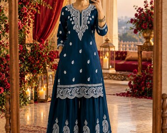 May include: A deep blue kurta and sharara set featuring intricate white embroidery. The knee-length tunic has three-quarter sleeves and a split neckline, while the wide-leg trousers feature a matching ornate paisley border at the hem.