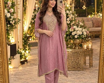 May include: A mauve-colored tunic with a V-neckline featuring intricate gold embroidery and matching straight-leg trousers. The tunic has wide, short sleeves and gold trim along the edges, creating a coordinated two-piece outfit.