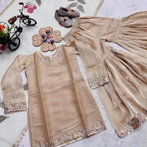 May include: A beige long-sleeved tunic and matching wide-leg trousers set featuring delicate silver embroidery and floral beadwork along the neckline, cuffs, and hem. The set is accompanied by a pair of beige ballet flats with bow accents.