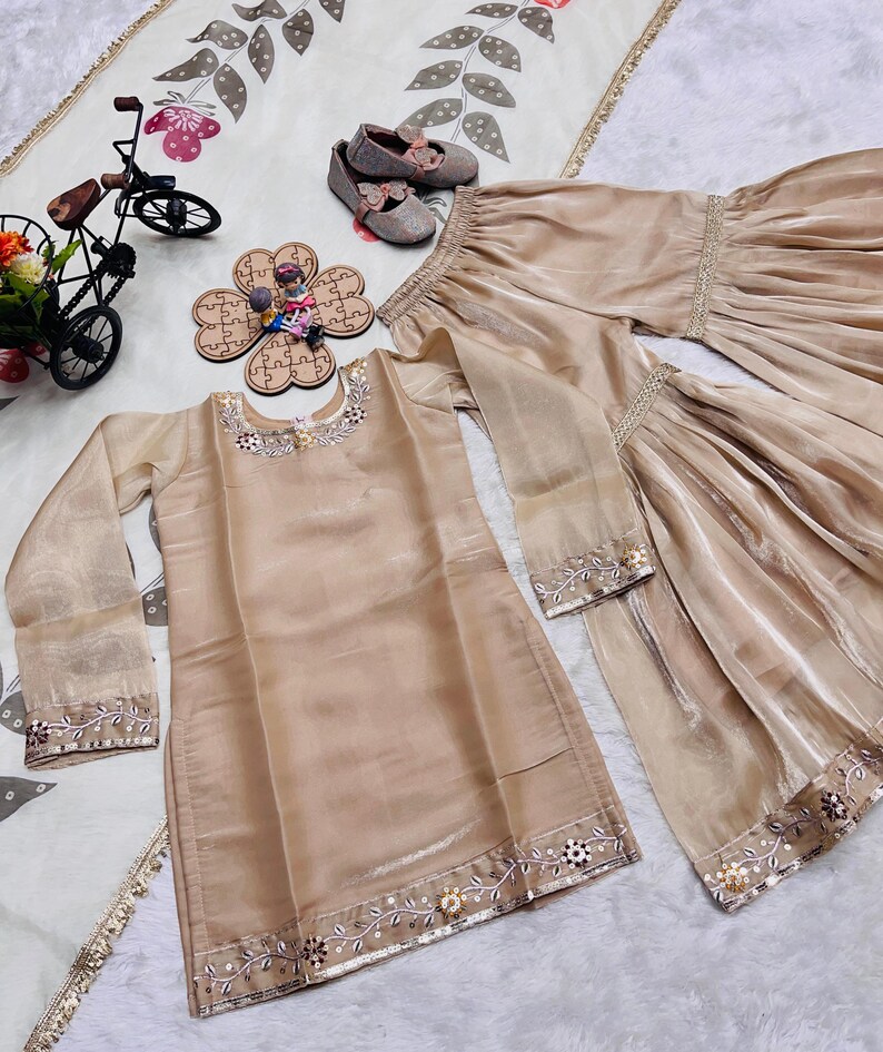 May include: A beige long-sleeved tunic and matching wide-leg trousers set featuring delicate silver embroidery and floral beadwork along the neckline, cuffs, and hem. The set is accompanied by a pair of beige ballet flats with bow accents.