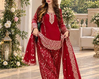May include: A deep red three-piece outfit consisting of a long-sleeved tunic, matching trousers, and a sheer dupatta. The garments feature intricate gold embroidery along the hemlines, neckline, and sleeves, with a scalloped border design.