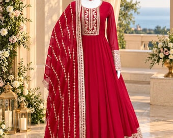 May include: A floor-length red gown with long sleeves, featuring intricate gold embroidery around the neckline, cuffs, and hem. The dress is paired with a matching red dupatta that has a gold embroidered border and vertical patterns.