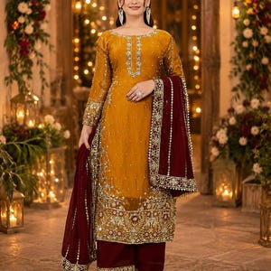 May include: A mustard yellow long-sleeved tunic featuring intricate silver embroidery and beadwork, paired with deep maroon wide-leg trousers and a matching maroon dupatta with a wide, heavily embellished gold and silver border.