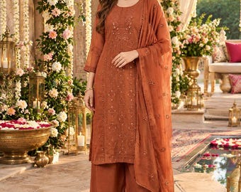 May include: A rust-colored three-piece outfit consisting of a long-sleeved tunic with intricate embroidery and sequin detailing, wide-leg trousers, and a matching sheer dupatta draped over one shoulder, all in a coordinated monochromatic tone.