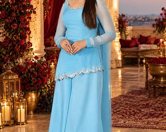 May include: A light blue three-piece ensemble consisting of a long-sleeved tunic with silver scalloped embroidery at the hem and neckline, matching wide-leg trousers, and a sheer light blue dupatta scarf draped over the shoulders.