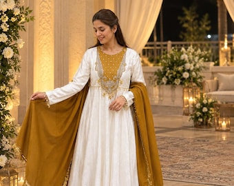 May include: A white long-sleeved dress with a mustard yellow chest panel featuring silver embroidery and pearl accents. The dress is paired with matching white wide-leg trousers and a mustard yellow shawl with gold trim and sequin details.